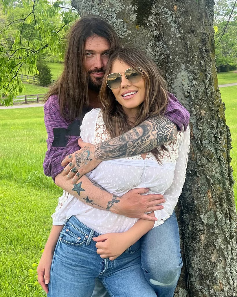 Billy Ray Cyrus and Elizabeth Hurley holding each other under a tree